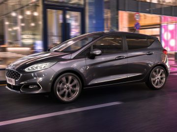 Een moderne grijze Ford Fiesta hatchback-auto die 's nachts door een stedelijk gebied rijdt.