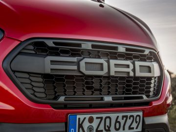 Close-up van de grille van een rood Ford Transit Trail-voertuig met het Ford-logo.
