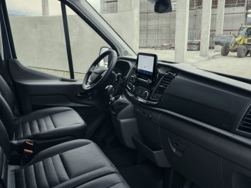 Binnenaanzicht van de voorcabine van een modern Ford Transit Trail-voertuig, met de nadruk op het dashboard, het stuur en het infotainmentsysteem.