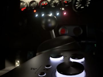 Vliegtuigcockpit bij nacht met verlichte wijzerplaten en stuurknuppel, die doet denken aan een PlayStation 5 Gran Turismo 7-raceopstelling.
