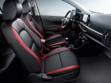 Modern Kia Picanto-interieur met zwarte en rode bekleding, voorzien van touchscreen-infotainmentsysteem en handgeschakelde versnellingsbak.