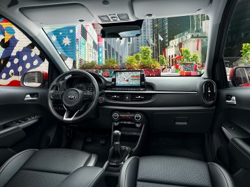 Binnenaanzicht van een moderne Kia Picanto met een touchscreen-infotainmentsysteem, met uitzicht op een levendige stadsstraat.