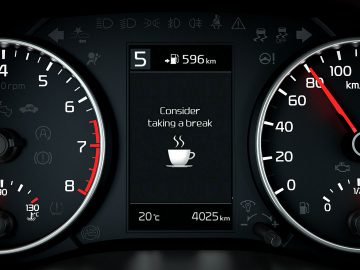 Kia Picanto-dashboard met snelheidsmeter, brandstofbereik en een herinnering om een pauze te nemen met een koffiekopje-pictogram.