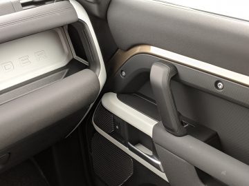 Interieurdetail van een Land Rover Defender met de deurgreep, het opbergvak en het luidsprekerrooster.