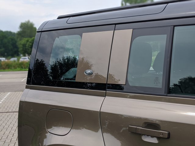 Zijaanzicht van een Land Rover Defender met getinte ramen en een zichtbare tankdop.