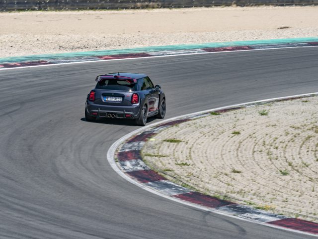 Een MINI John Cooper Works GP 2020 racet op een circuit met een kleine bocht en stoepranden aan de zijkant.