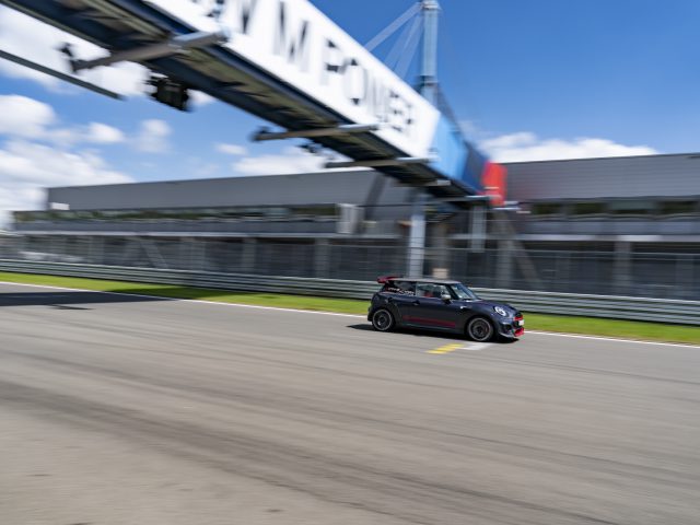Een zwarte MINI John Cooper Works GP 2020 die over een racecircuit rijdt met een bewegingsonscherpte-effect dat de snelheid benadrukt.