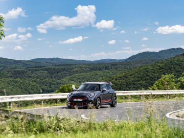 Een zwarte MINI John Cooper Works GP 2020 rijdend op een bochtige weg met een schilderachtig landschap op de achtergrond.