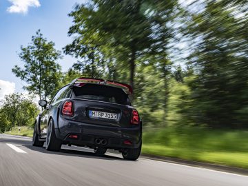Zwarte MINI John Cooper Works GP 2020 auto rijdt op een weg met bewegingsonscherpte die de snelheid aangeeft.