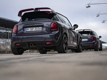 Twee MINI John Cooper Works GP 2020-auto's geparkeerd op een asfaltoppervlak, met de nadruk op het sportieve ontwerp van de achterkant van het dichtstbijzijnde voertuig.