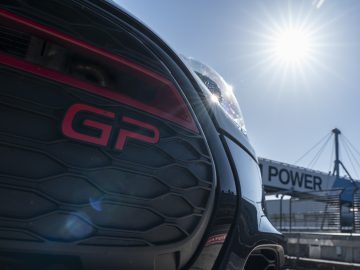 Een close-up van de achterkant van een MINI John Cooper Works GP 2020-auto met een 'gp'-badge, onder een heldere hemel en de zon helder schijnt.