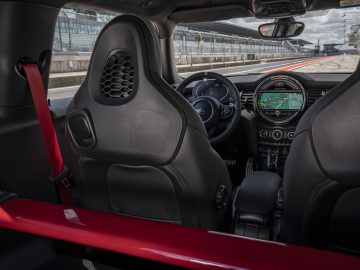 Binnenaanzicht van de MINI John Cooper Works GP 2020 sportwagen, met de focus op de bestuurdersstoel, het dashboard en het stuur, met een racecircuit door de voorruit.