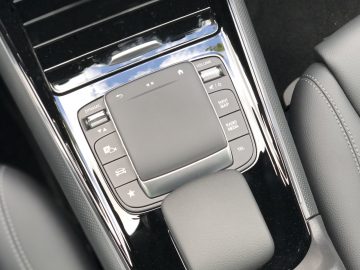 Close-up van het interieur van de middenconsole van een Mercedes-Benz GLA met een touchpad, volumeregeling en andere multimediaknoppen.