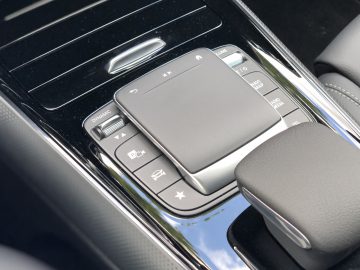 Binnenaanzicht van de middenconsole van de Mercedes-Benz GLA met een touchpad, versnellingspook en verschillende bedieningsknoppen.