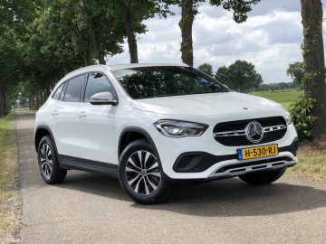 Een witte Mercedes-Benz GLA geparkeerd aan de kant van een landweg met bomen op de achtergrond.