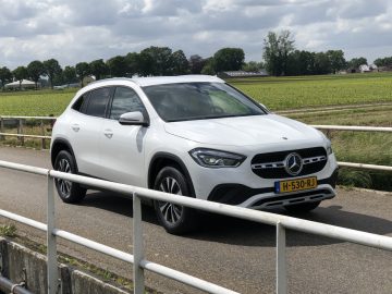 Een witte Mercedes-Benz GLA SUV geparkeerd naast een landelijke weg met velden op de achtergrond.