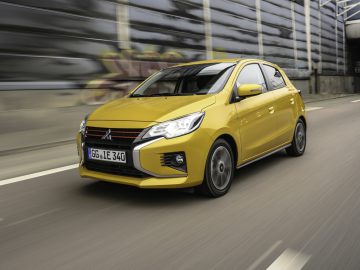 Een gele Mitsubishi hatchback-auto die op een snelweg rijdt.