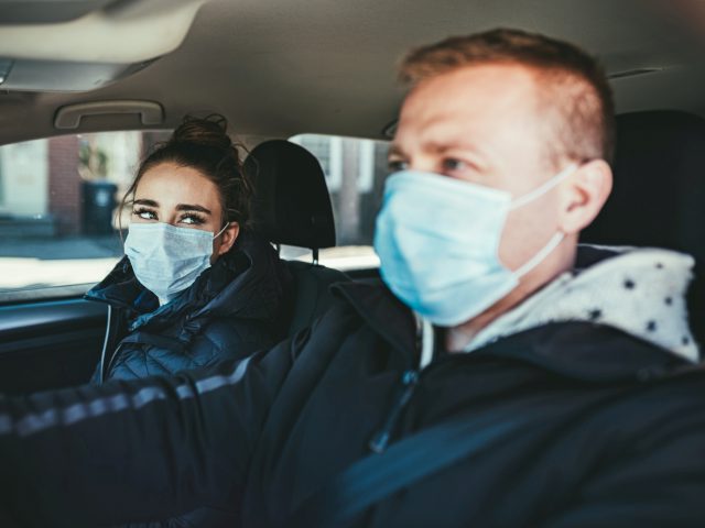 Twee mensen die beschermende maskers dragen en afschermen in een auto.