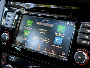 Auto-infotainmentscherm in een Nissan Qashqai N-TEC met radio- en menuopties en een klok die aangeeft dat het 19.30 uur is.