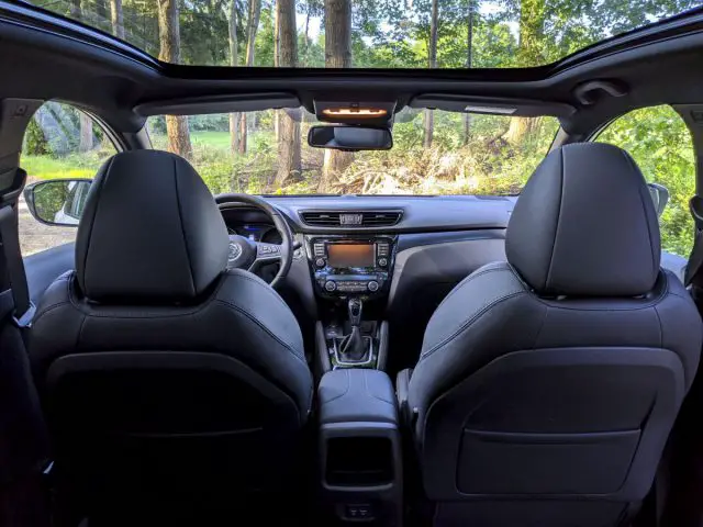 Binnenaanzicht van een Nissan Qashqai N-TEC vanaf de achterbank, met zwartleren stoelen, een middenconsole en een dashboard bij daglicht.