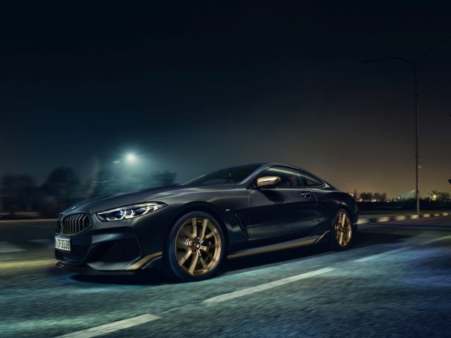 Een strakke zwarte BMW 8-serie coupé die 's nachts over een stadsweg rijdt met verlichte straatlantaarns op de achtergrond.