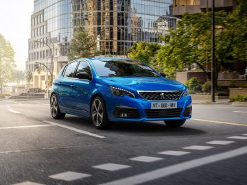 Blauwe Peugeot 308 compacte auto rijden op een stedelijke straat.