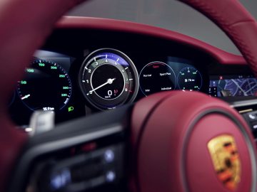 Binnenaanzicht van het dashboard van een 911 Targa 4S Heritage Design Edition-sportwagen met digitale displays en een rood stuur met een Porsche-embleem.