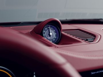 Close-up van het dashboard van een 911 Targa 4S Heritage Design Edition-auto met een roodleren dashboard met een enkele analoge klok.