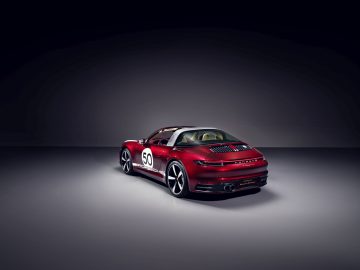 Een rode 911 Targa 4S Heritage Design Edition-sportwagen met het nummer 50 op de deur, tentoongesteld onder een spotlight.