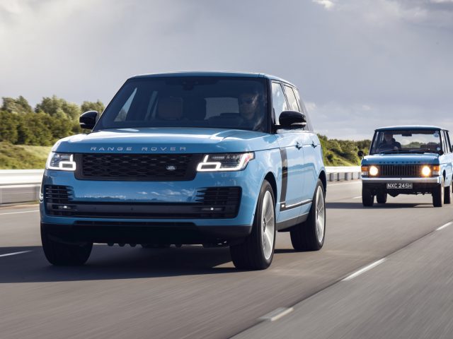Een blauwe moderne Range Rover Fifty leidt een ouder model Range Rover op een zonovergoten snelweg.