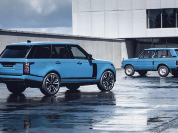 Twee generaties blauwe Range Rovers, de moderne Fifty en vintage, geparkeerd op nat beton.