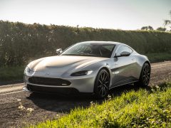 Zilveren Aston Martin Revenant geparkeerd langs de weg met groen op de achtergrond.
