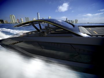 Een strakke zwarte Tecnomar voor Lamborghini 63 speedboot die over het water vaart met de skyline van een stad op de achtergrond.