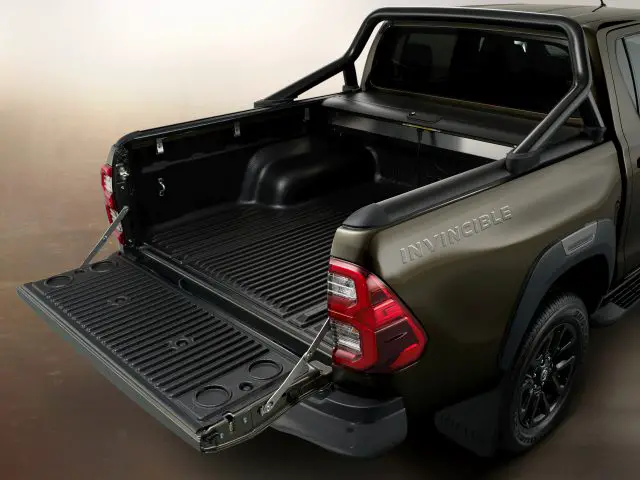 Olijfgroene Toyota Hilux pick-up met een open achterklep en een leeg bed, op de markt gebracht als 'onoverwinnelijk'.