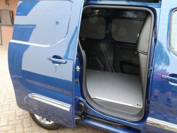 Een blauwe Toyota PROACE City-bestelwagen met de zijdeur open, waardoor een lege laadruimte met een grijs interieur zichtbaar wordt.
