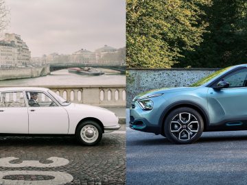 Een vintage Citroën C4 geparkeerd in een stadsstraat met links een rivier en brug op de achtergrond; een moderne blauwe SUV geparkeerd nabij het gebladerte aan de rechterkant.