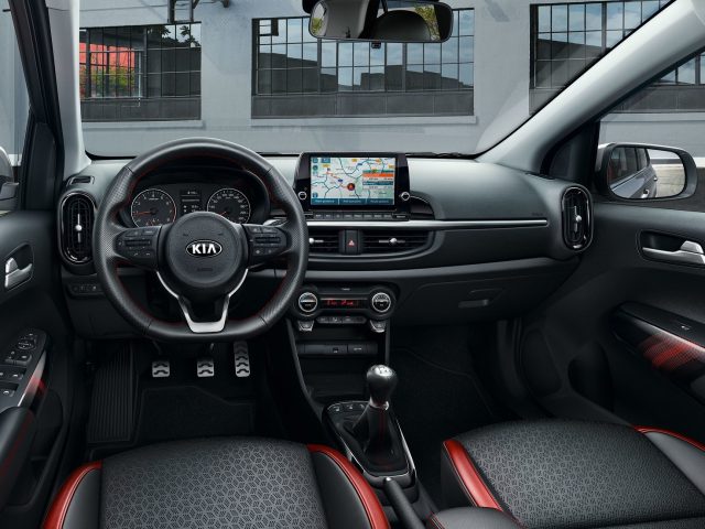 Modern auto-interieur met een Kia Picanto-stuur, touchscreen-infotainmentsysteem en tweekleurige rode en zwarte bekleding.