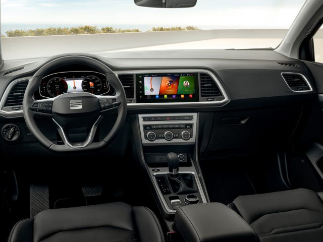 Binnenaanzicht van een moderne Seat Ateca met een digitaal displaydashboard en infotainmentsysteem, stuurwiel met logo en lederen stoelen.