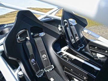 Close-up van zwarte racestoelen met harnassen in een Ariel Nomad R, met de nadruk op ingewikkelde stoeldetails en veiligheidsgordelsluitingen.