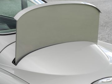 Close-up van een verhoogd zilverkleurig cabriodak dat gedeeltelijk achter de stoelen van een Aston Martin DB5 Goldfinger is teruggetrokken.