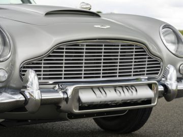 Close-up van de grille en koplampen van een zilveren Aston Martin DB5 Goldfinger Continuation, waarbij het klassieke ontwerp en de glanzende chromen details goed te zien zijn.