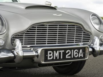 Close-up van een klassieke zilveren Aston Martin DB5 Goldfinger Vervolg met het kenteken "bmt 216a", met de nadruk op de grille en dubbele koplampen.