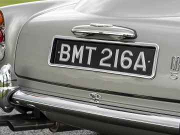 Close-up van de achterkant van een klassieke zilveren Aston Martin DB5 met een Brits kenteken 'BMT 216A', achterlichten en chromen bumper.