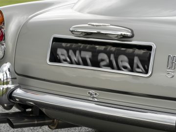 Close-up van de achterkant van een Aston Martin DB5 Goldfinger Continuation met een chromen kentekenplaathouder met de kentekenplaat "bmt 216a" en klassieke achterlichten.