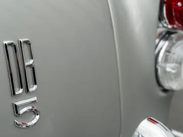Close-up van een zilveren Aston Martin DB5 Goldfinger Vervolg met een chroom "r8 5" embleem en een deel van een achterlicht zichtbaar.