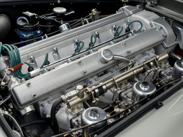 Een close-up van een Aston Martin DB5 Goldfinger Continuation-motor met zichtbare metalen componenten en ingewikkelde details.