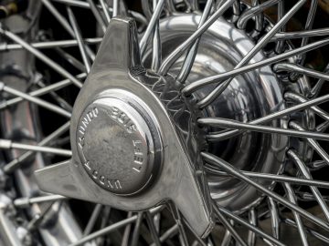 Close-up van een verchroomde motorfietswielnaaf met gedetailleerde spaken en een middenkap met het Aston Martin-logo.