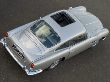 Bovenaanzicht van een klassieke Aston Martin DB5 Goldfinger Vervolg met strakke rondingen en chromen details geparkeerd op een asfaltoppervlak.