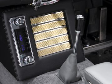 Interieur van een Aston Martin DB5 Goldfinger Vervolg met een retroradio en versnellingspook met een geperforeerd metalen paneel.