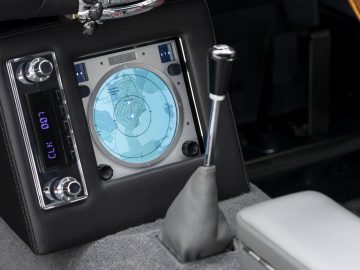 Interieur van een Aston Martin DB5 Goldfinger Vervolg met een digitaal navigatiescherm, versnellingspook en klimaatregelingsdisplay.